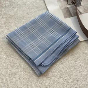 Detail of blue and white checkered cotton square scarf with fine stitched edges on plush surface