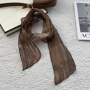 Brown plaid skinny scarf and leather bag on white jacquard fabric lifestyle scene