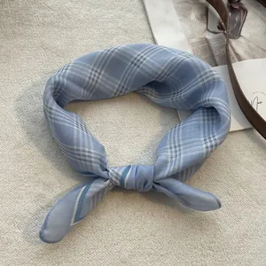 Detail of light blue checkered cotton scarf tied in a knot on soft white texture