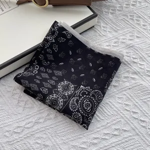 Detail shot of a black silk scarf with white paisley patterns on textured white background
