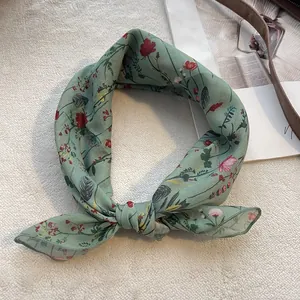 Dettaglio di sciarpa in chiffon verde chiaro a fiori annodata su sfondo di peluche bianco
