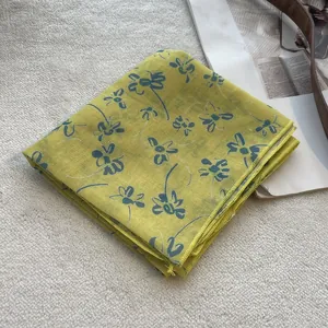 Detailed close-up of folded yellow floral cotton scarf with blue flowers on plush rug