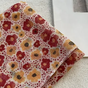 Dettaglio di un foulard in lino floreale con fiori rossi e gialli e bordi orlati bianchi