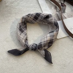 Detail van geruite zijden sjaal met zachte stoftextuur en geknoopte styling op wit tapijt