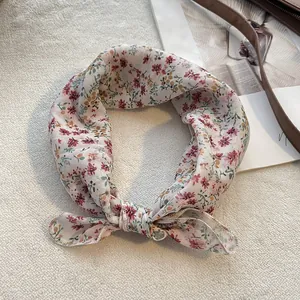 Dettaglio di un foulard quadrato in cotone e lino a fiori annodato su sfondo morbido