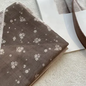 Detail van een bruine vintage bloemensjaal met geruite rand op een zachte witte ondergrond