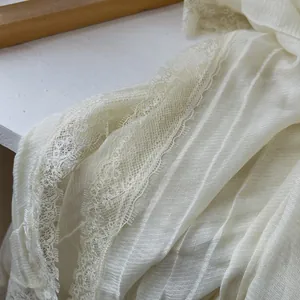 Detail of cream cotton linen scarf showing vertical pleats and delicate eyelash lace trim