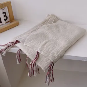 Beige cotton linen shawl with colorful handmade fringe tassels on a soft wrinkled fabric