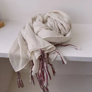 Detail of light beige cotton linen scarf featuring colorful bohemian tassel edges