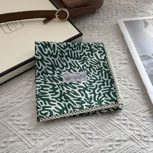 Detail of 100% cotton square scarf featuring green abstract print and white lace trim
