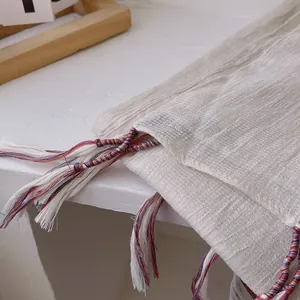 Detailed macro view of beige linen shawl featuring colorful braided tassels and pleated texture