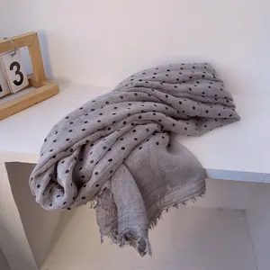 Detailed texture of grey linen scarf featuring black polka dots and natural frayed edges