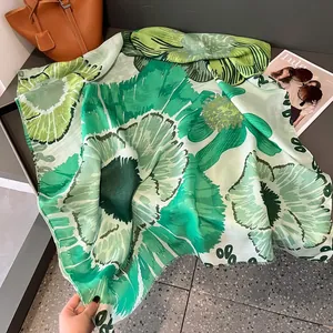 Détail d'un châle en soie à fleurs vertes posé à côté d'un magazine de mode chic