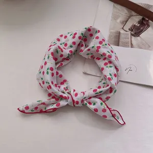 Close-up of white cotton headscarf featuring red cherry print and a knotted bow detail