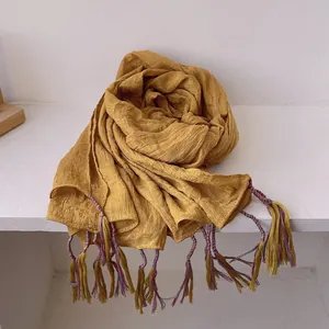 Macro detail of mustard cotton linen scarf featuring colorful handmade fringe tassels