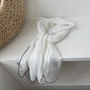 Detail of white thin silk scarf with black contrast wavy hem and 100% polyester texture