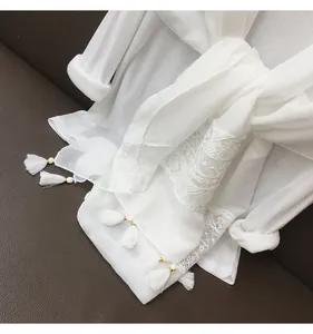 Detail of white thin ethnic shawl with lace patchwork and white tassel ornaments