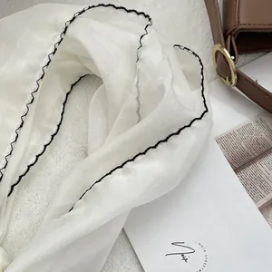 Detail of white thin silk scarf featuring black scalloped embroidery and lightweight texture