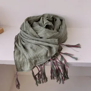 Detail of light green cotton linen scarf showing delicate tassels and red blue thread wrapping