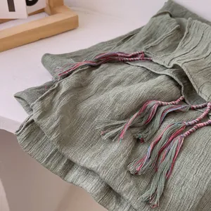 Close-up of grass green cotton linen scarf with colorful braided tassels and crinkle texture