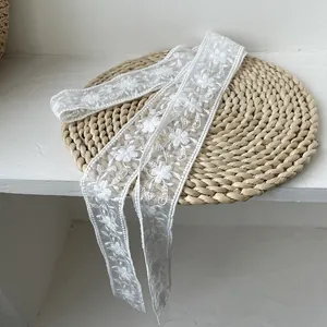 Détail d'une écharpe en dentelle blanche avec broderies florales fines et bordures ondulées