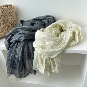 Dettaglio ravvicinato di sciarpe leggere in cotone e lino con bordo in pizzo grigio e crema