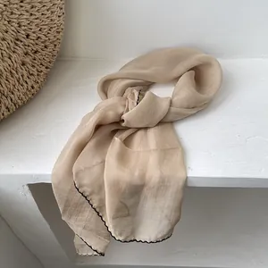 Detail of light beige chiffon scarf with contrast black wavy stitched edges for women