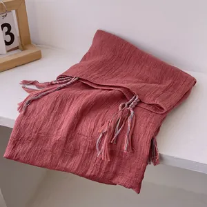Detail of brick red cotton linen scarf with colorful braided tassels and wrinkled texture