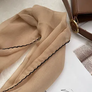 Macro detail of champagne silk scarf with black wavy edge stitching on soft background