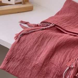 Macro detail of dark red linen scarf showing soft wrinkled texture and colorful tassels