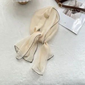Close-up of cream chiffon scarf with black wavy edges on white plush background