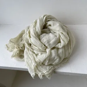 Dettaglio della sciarpa in cotone e lino beige con bordi in pizzo e trama del tessuto