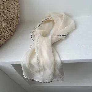 Detailed texture of lightweight beige chiffon scarf with elegant black scalloped edges