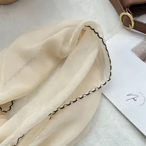 Detailed close-up of light beige silk scarf with black wavy contrast stitching and soft texture
