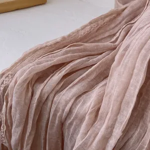 Dettaglio di sciarpa plissettata rosa chiaro con bordo in pizzo e trama in lino morbido