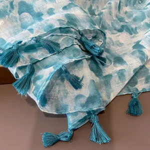 Detailed macro shot of light blue tie-dye linen scarf featuring elegant fringe tassels