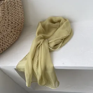 Detail of light green chiffon scarf with white picot trim next to a woven straw bag
