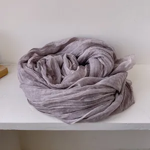 Dettaglio di una sciarpa di lino viola chiaro con bordi in pizzo su legno bianco
