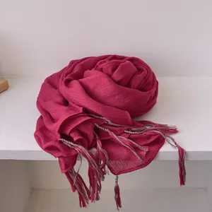 Detail of dark rose linen cotton scarf with colorful tassels on white wood