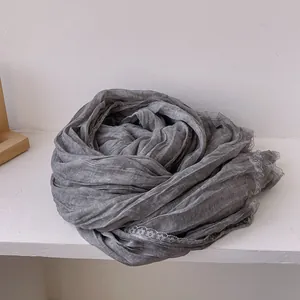 Dettaglio della sciarpa di lino grigio con trama a pieghe e bordo in pizzo bianco