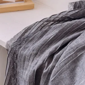 Dettaglio del tessuto plissettato grigio della sciarpa con bordo in pizzo nero delicato