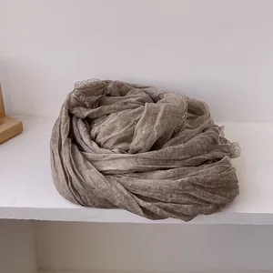Dettaglio di sciarpa in cotone e lino beige scuro con pizzo elegante e trama a pieghe