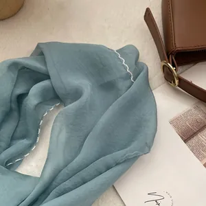Detail view of light blue sheer scarf with white wavy embroidered edges on a velvet background