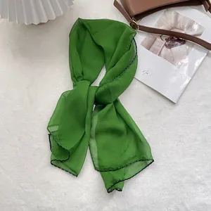 Detailed view of dark green silk scarf with black contrast stitching and soft texture