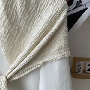 Detail of crinkled cream cotton linen scarf featuring delicate eyelash lace trim edges