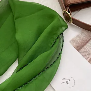 Close-up of lightweight emerald green chiffon scarf with detailed black stitched edges