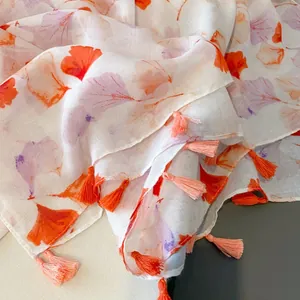 Detail of white cotton shawl featuring orange ginkgo leaf prints and handmade tassels