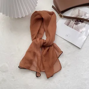 Detail of thin caramel brown silk scarf with decorative black wavy stitched edges