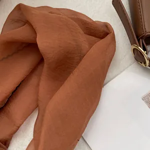 Detailed texture of thin caramel silk scarf draped over a brown leather bag strap