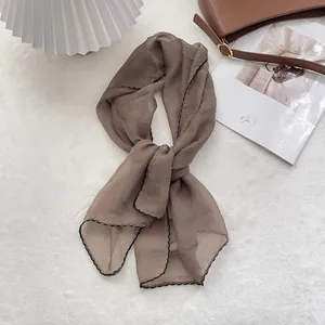Detailed view of taupe chiffon scarf with elegant black scalloped edge on white texture